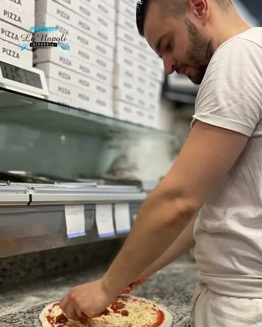 Le pizzaiolo du Napoli garnit une pizza derrière le comptoir